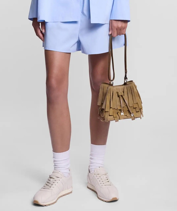 Accessories Image of a woman wearing a fringed handbag, shorts, a blue shirt, and a pair of beige sneakers